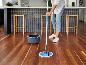 A person mopping wooden floors in a kitchen with a mop and a bucket next to it.
