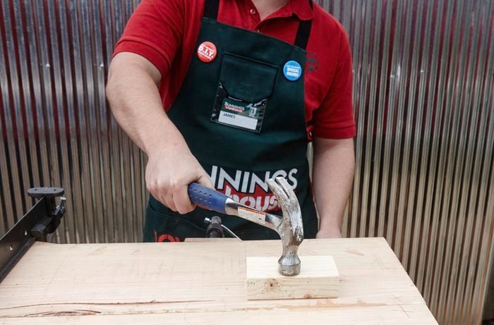 A person hammering a piece of pine sitting on top of a length of hardwood