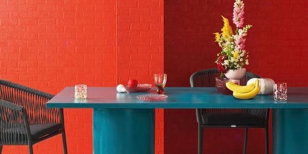 Fruits and a flower vase on top of a green table in a living room.