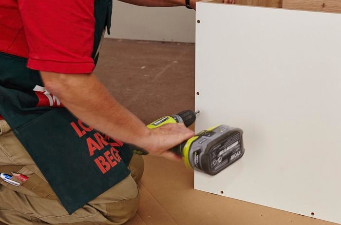 A person assembling a cabinet using a cordless driver