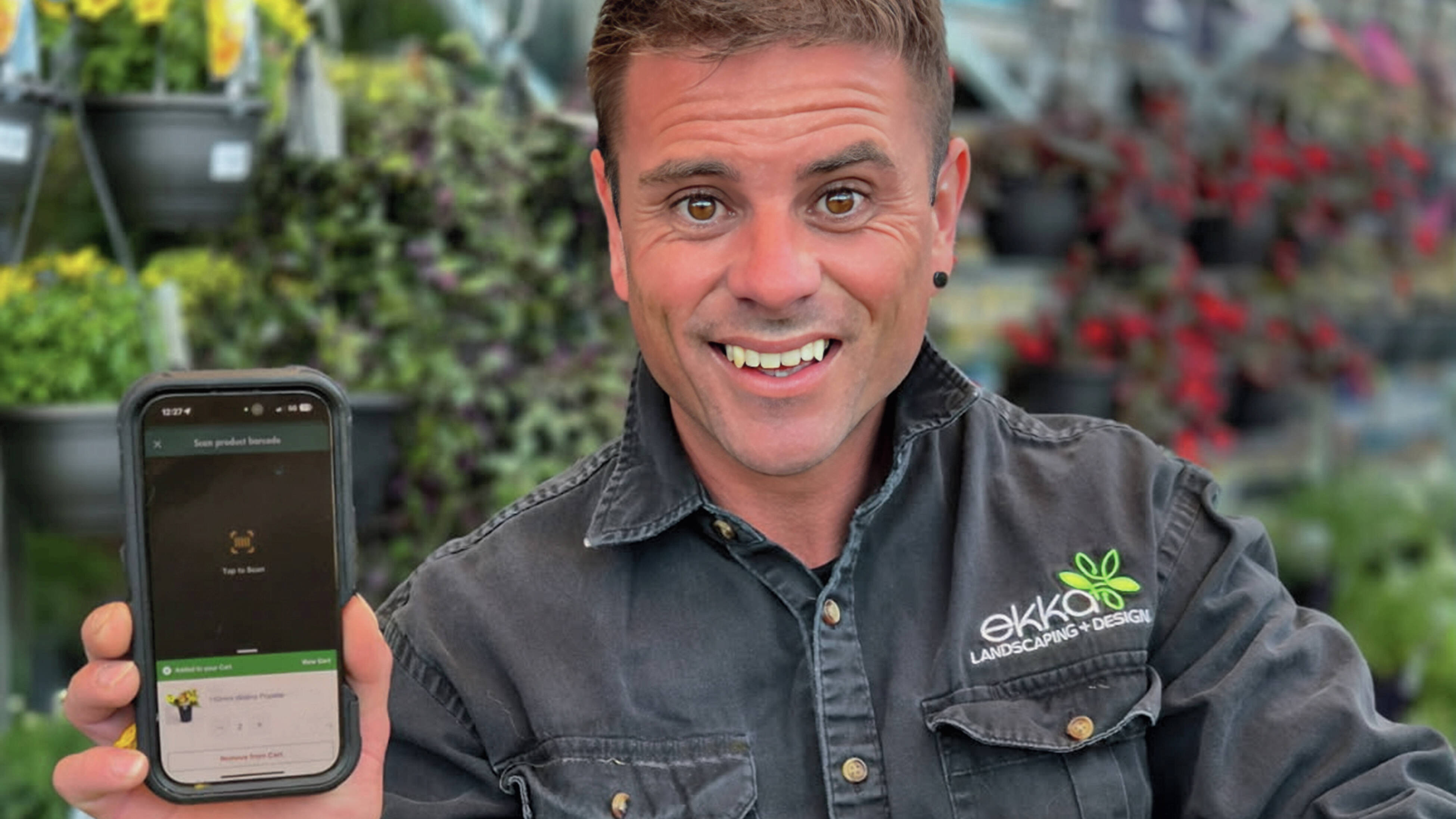 Close up of landscaper Kayne Hunter holding a smartphone showing the Bunnings PowerPass app in the garden section at Bunnings.