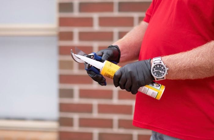 A person cutting the tip of the caulking tube.