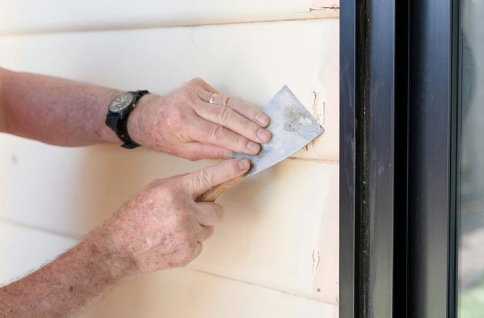 A person scraping weatherboards with a paint scraper