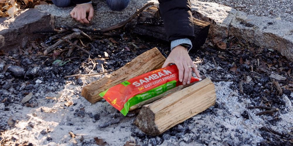 Samba
  Firelog (3180823) being placed beneath two pieces of firewood to start the
  fire