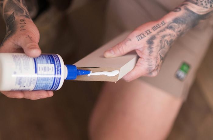 A person is applying strong construction adhesive to the back of the skirting board while holding it steady.