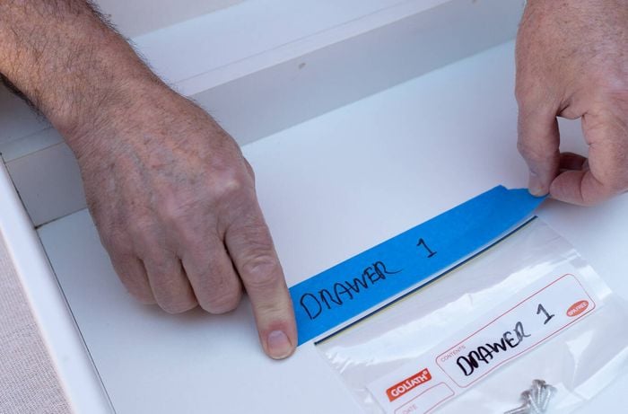 A person is labeling kitchen cabinet doors with masking tape and storing screws in labeled bags