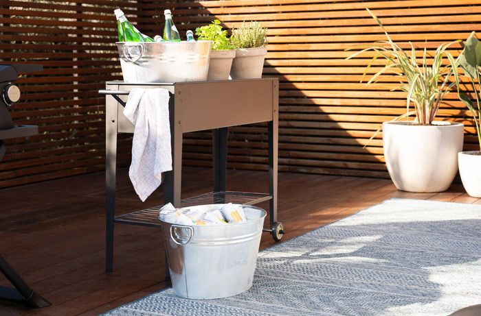 Outdoor drinks station with bottled beverages, herbs and ice buckets on a serving cart.