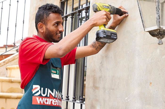 Person pinching the outside of a screw while drilling the screw into a wall