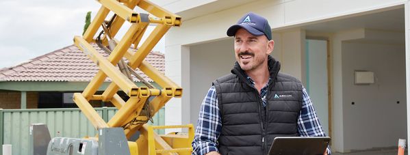 Trade professional holding a tablet beside a scissor lift at a residential construction site.