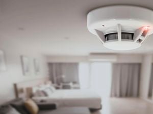 Smoke alarm attached to ceiling with red light on.