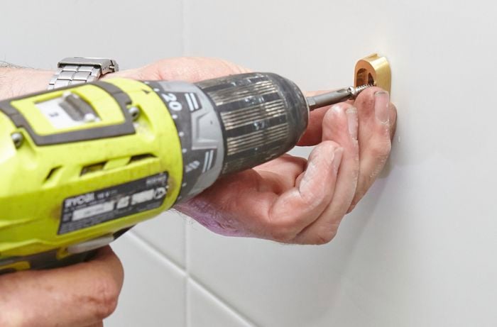 A person attaching towel rail fittings to a tile wall using a cordless drill