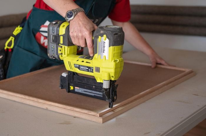 A person nailing the wood trim using a nail gun.