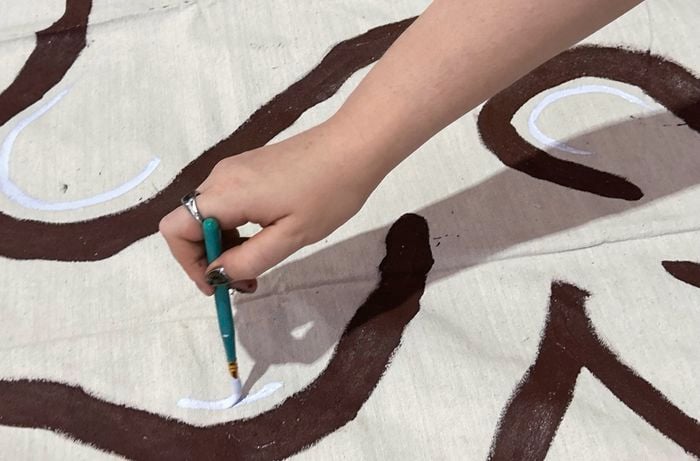 A close up of a hand painting a blue and brown swirl design for the bench seat cover on a canvas drop sheet