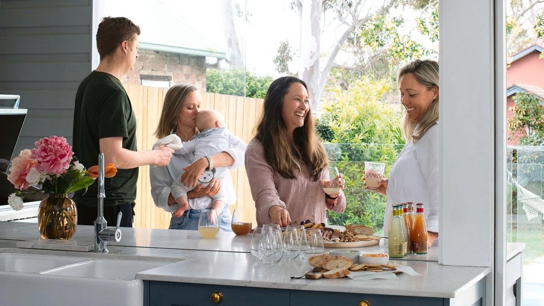 A group of people gathered around a kitchen chatting and laughing