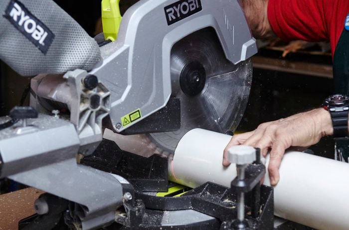 A person cutting a length of PVC pipe using a drop saw