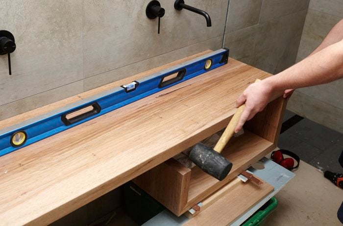 A person using a rubber mallet to tap a floating timber vanity into position in a bathroom 