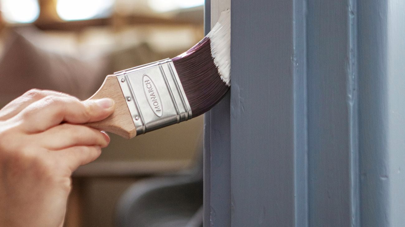 Hand holding a paintbrush and painting a white stripe onto a blue architrave