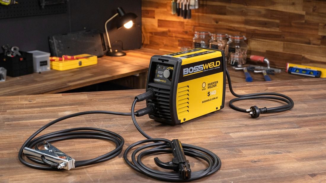 Arc welder and cords displayed on a timber workshop bench.