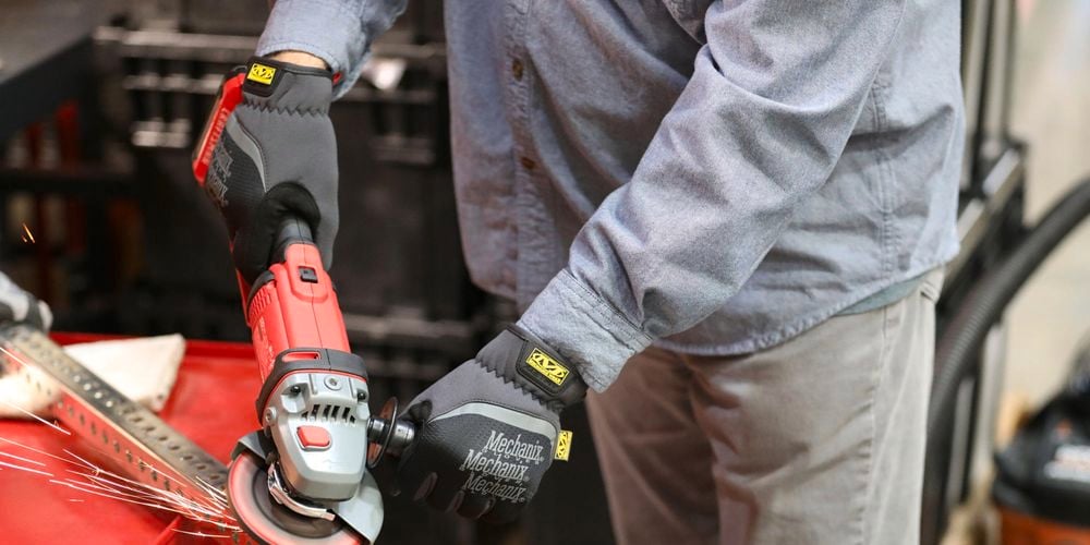 Person wearing gloves and using an angle grinder on a piece of steel