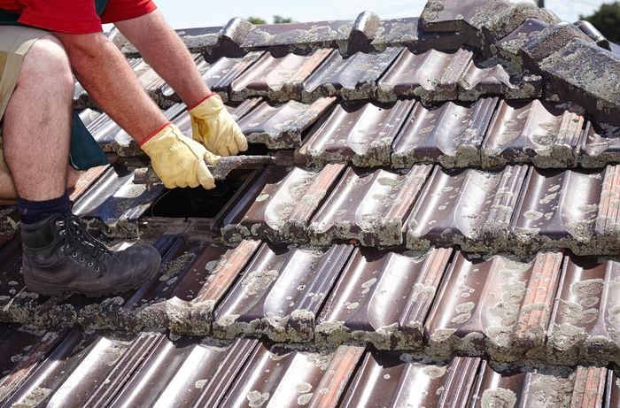 A person on a tiled roof replacing a roof tile