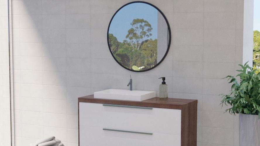Bathroom with black framed round mirror along with wash basin, plant and white wall tiles.