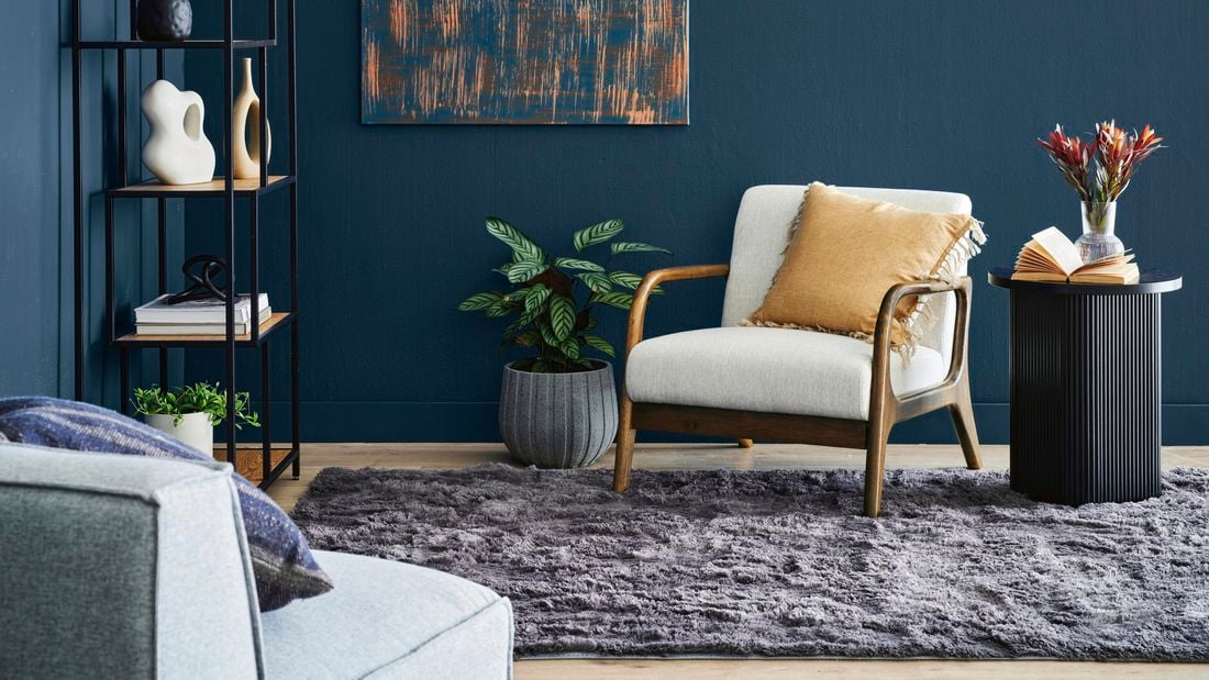 Close up shot of armchair in living room setting next to side table, plants and painting on wall.