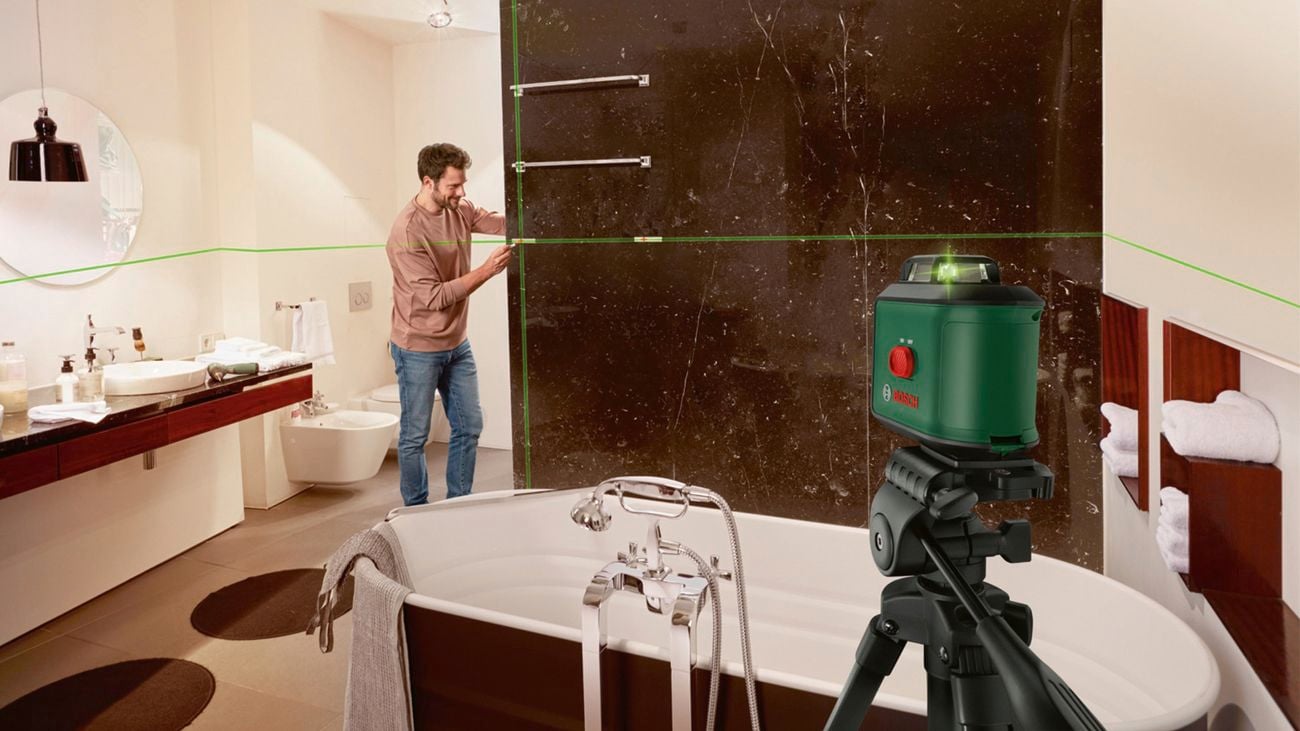 A man using a Bosch ‘Universal Level 360’ green beam line laser to measure fixtures in a bathroom