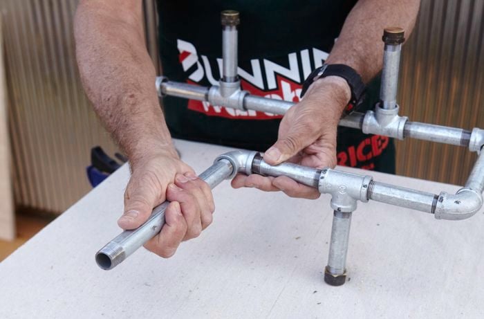 An ironing board storage rack being assembled from metal pipe