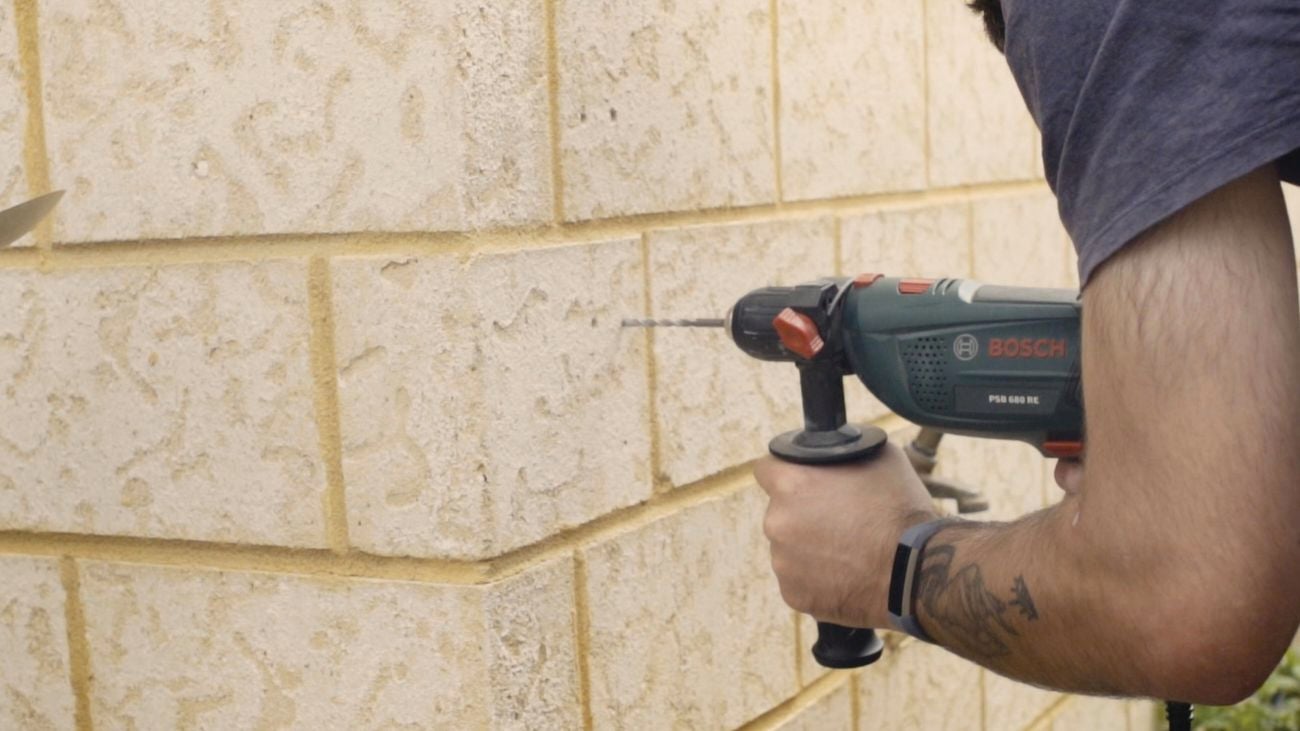 Person holding an electric drill to drill holes in an outdoor brick wall