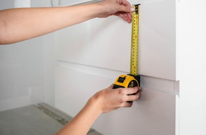 A tape measure being used to measure a white vanity