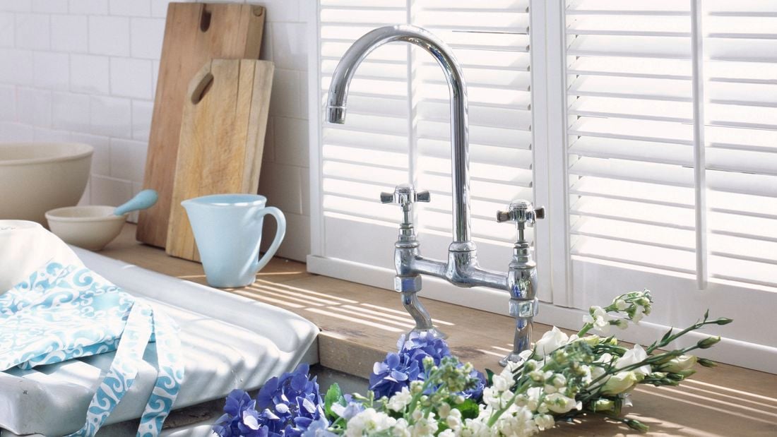 Close up of a kitchen sink and white shelves filled with blue and white dinnerware.