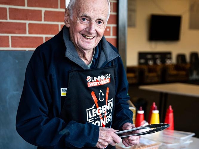 A gentleman standing behind a t barbecue that has sausages on it.
