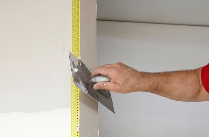 Person scraping over plaster on wall and external angles to smooth it out.