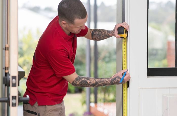 A Bunnings Team Member is measuring and marking a door frame with a tape measure and pencil to prepare it for installation