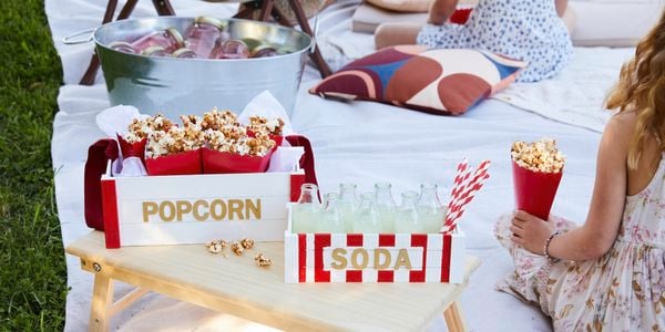 Soda and popcorn tray sitting on a bed tray while in a picnic style movie night is happening