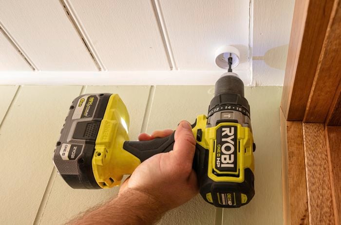 A person drilling the ceiling with a drilling machine.
