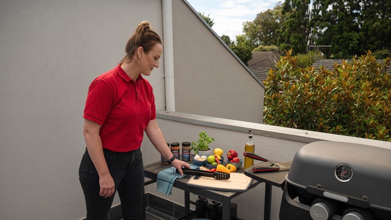 A woman keeping a tong on the table and a BBQ machine next to it.