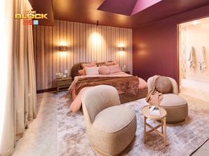Bedroom with plum-colored walls, upholstered bed, two beige chairs, and soft lighting.
