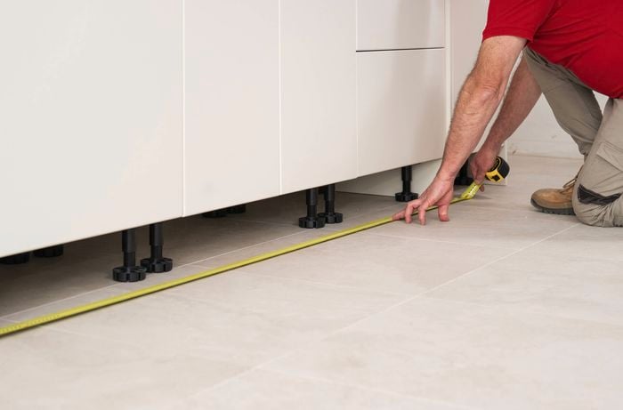 A person is using a tape measure to measure the length of each section where a kickboard will be installed.