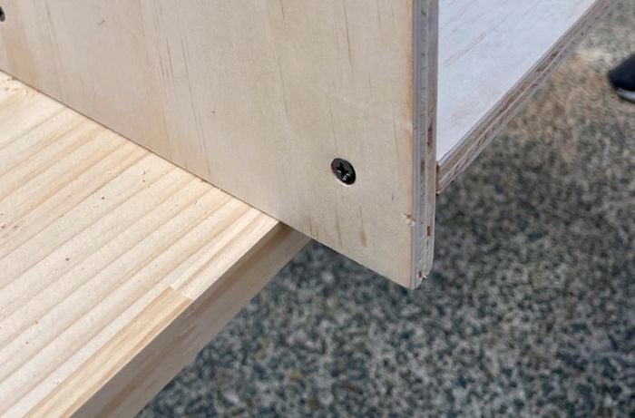 A panel of wood with two screws drilled into it perpendicular to another panel of wood