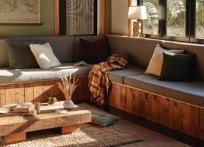 <p>Grey couch with grey curtains by the open window in a living room. Other furnishings like a coffee table, a white lamp and a large window are also featured</p>