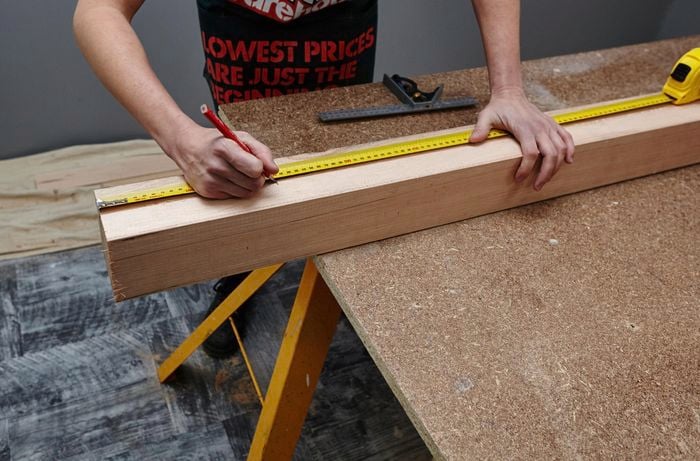 The post of a wooden coat rack being measured for cutting with a pencil and tape measure