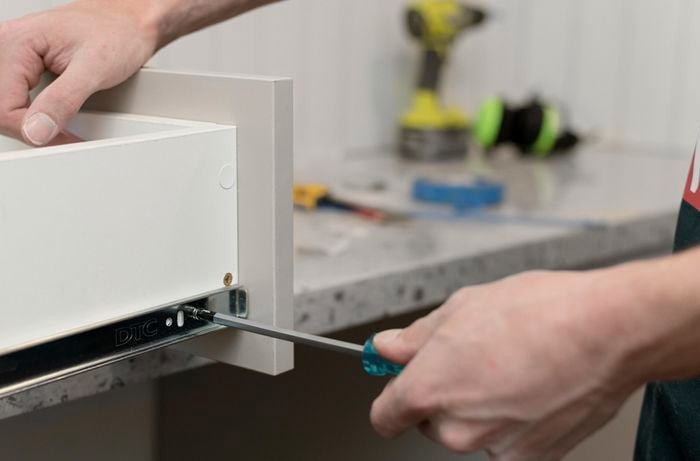 Using screwdriver to add tracks to a drawer.