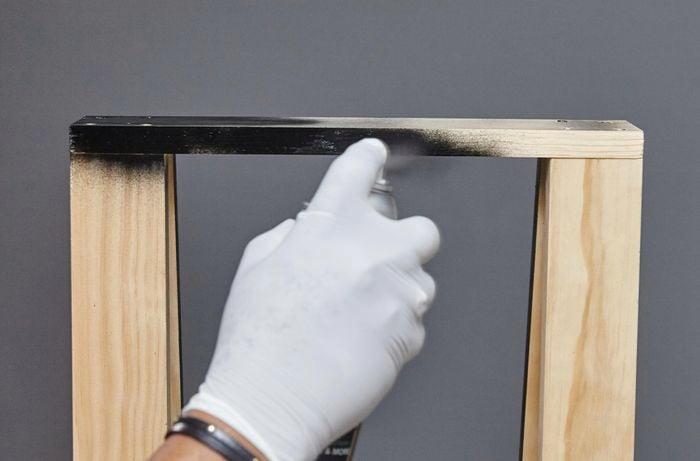 A person spray painting timber black