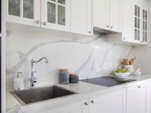 Modern white bathroom with white cabinetry, marble look splashback and benchtop, electric stovetop and stainless steel tapware.