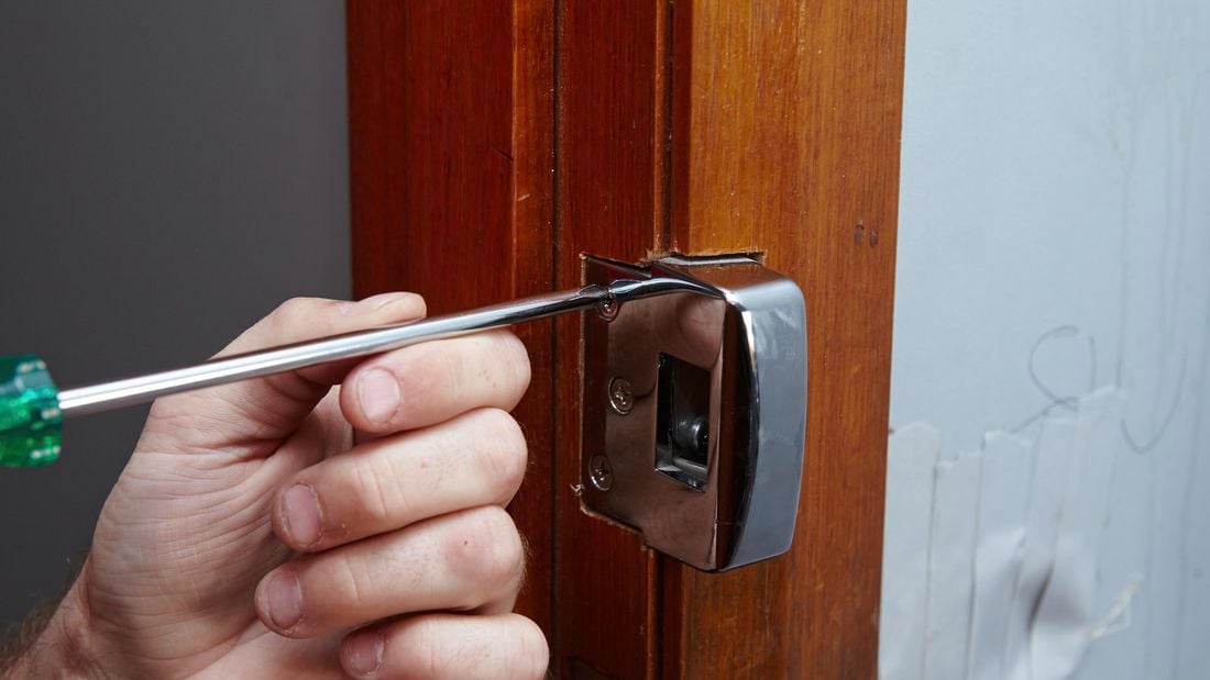 A door latch being unscrewed from a door jamb