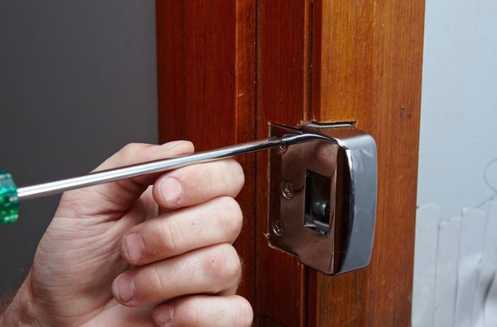 A door latch being unscrewed from a door jamb