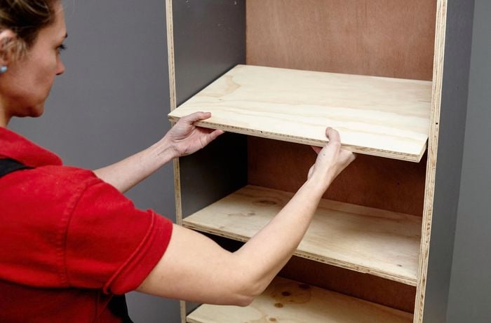 A person fitting a shelf into an open timber shelving unit