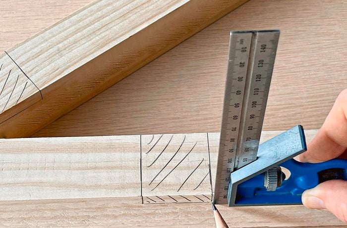 A person uses a combination square to measure and mark a piece of pine.