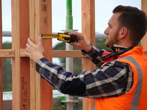 A construction worker measuring the width of a building frame